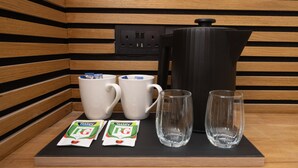 Une petite cuisine équipée d’une machine à café, de deux tasses blanches, de deux verres et de deux sachets de thé Tetley PG.