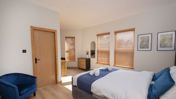 Une chambre à coucher avec un lit, une chaise bleue, une porte en bois, une commode et un miroir.