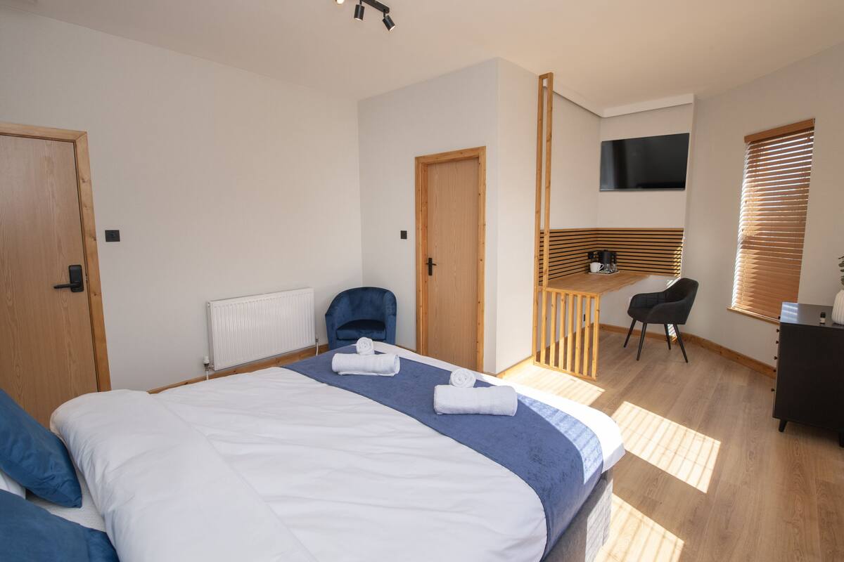 A modern hotel room with a large bed, a desk, a chair, and a TV mounted on the wall.