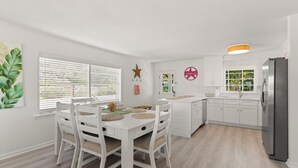 A modern kitchen with white cabinetry, a dining table with chairs, and a large refrigerator. - Toddy Cottage located on East Beach, sleeps 10 (St Simons Island)
