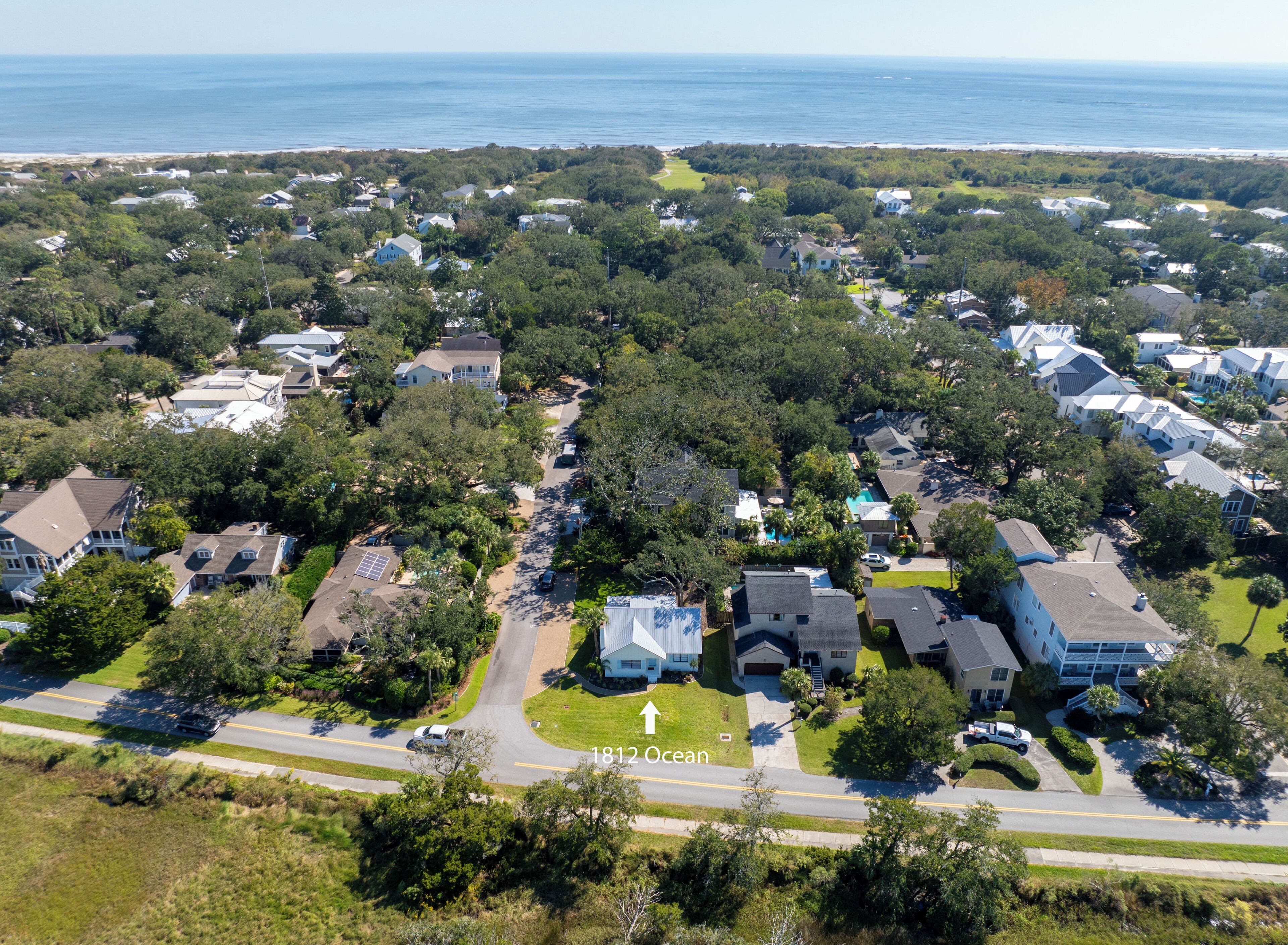 An aerial view of a residential area with houses, roads, and a beach in the background.