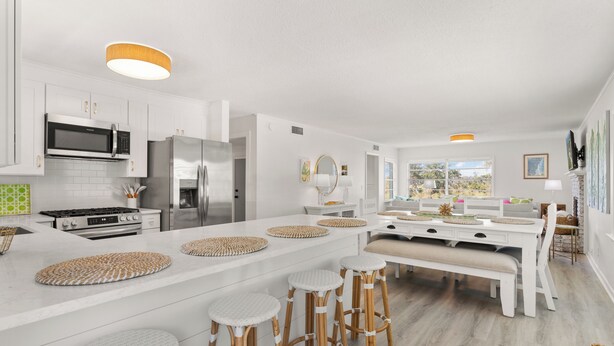 A modern kitchen with white cabinetry, stainless steel appliances, and a central island with stools. - Toddy Cottage located on East Beach, sleeps 10 (St Simons Island)