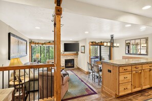 A spacious living area with a fireplace, wooden furniture, and large windows offering a view of the outdoors.