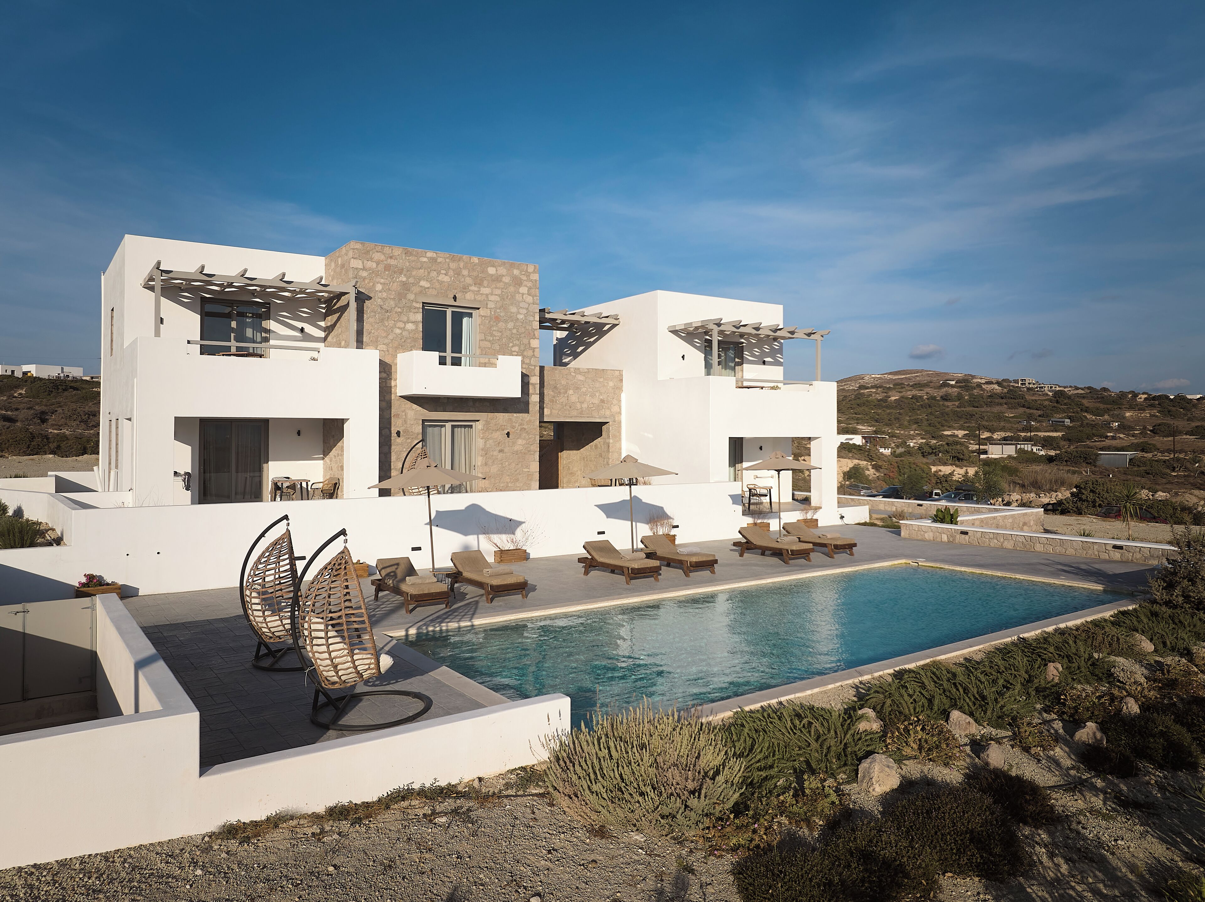 A modern villa with a pool, outdoor seating, and a view of the surrounding landscape.