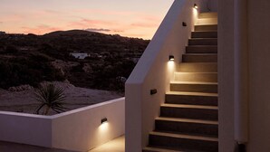 A modern staircase with built-in lighting, leading to a terrace with a view of a hilly landscape during twilight. - Kedros Milos Suites (Milos)