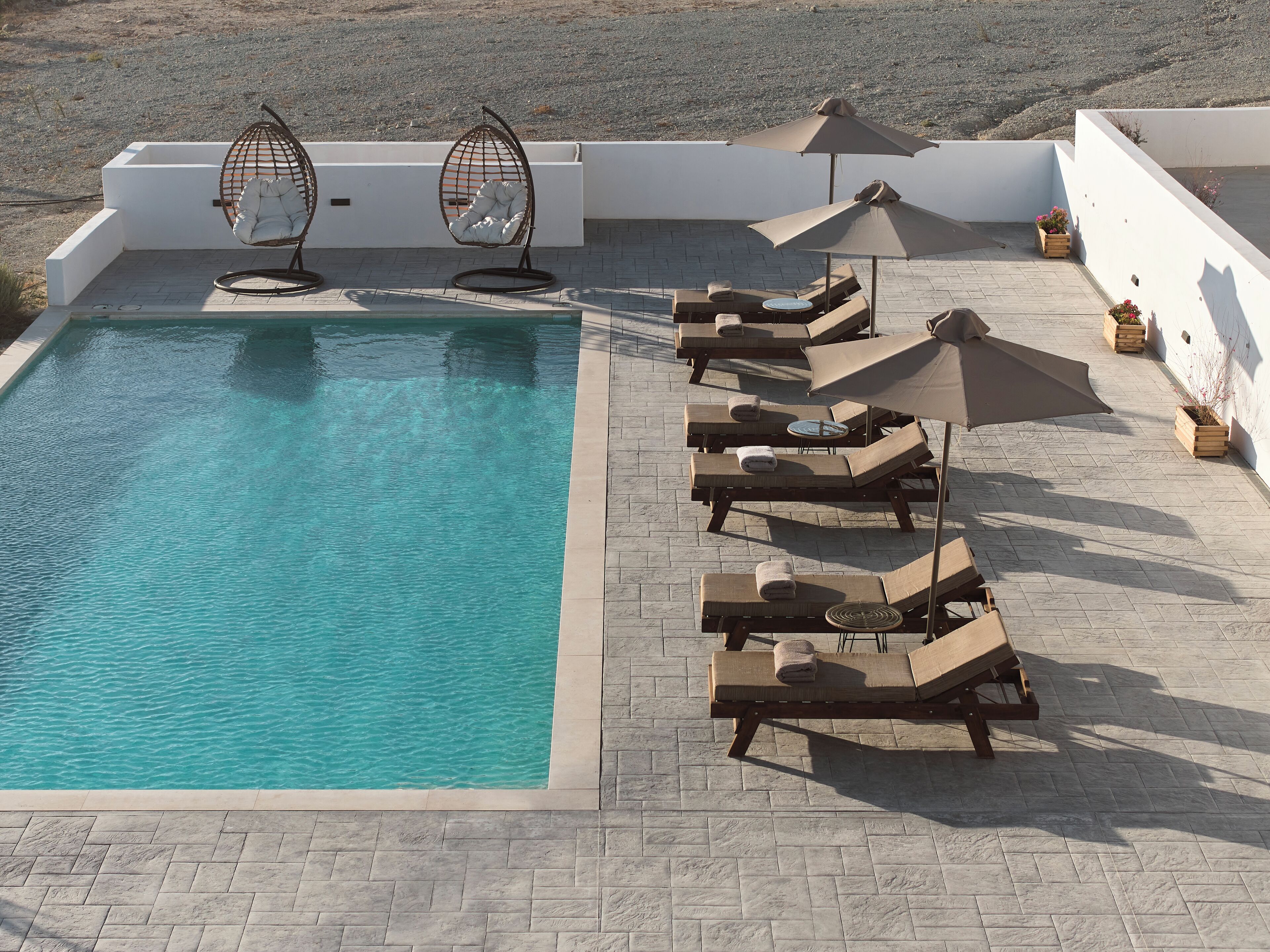 A pool area with lounge chairs, a hanging chair, and potted plants.