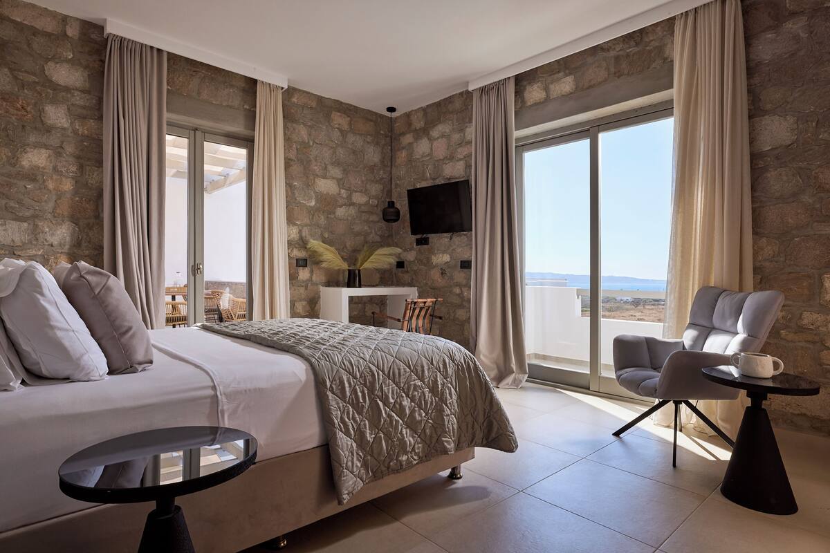 A bedroom with a large bed, a chair, a small table, and a TV mounted on the wall.