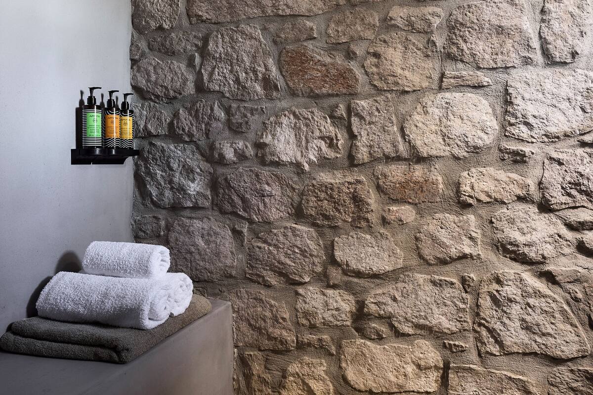A stone-walled bathroom with a shower, a shelf with toiletries, and towels.