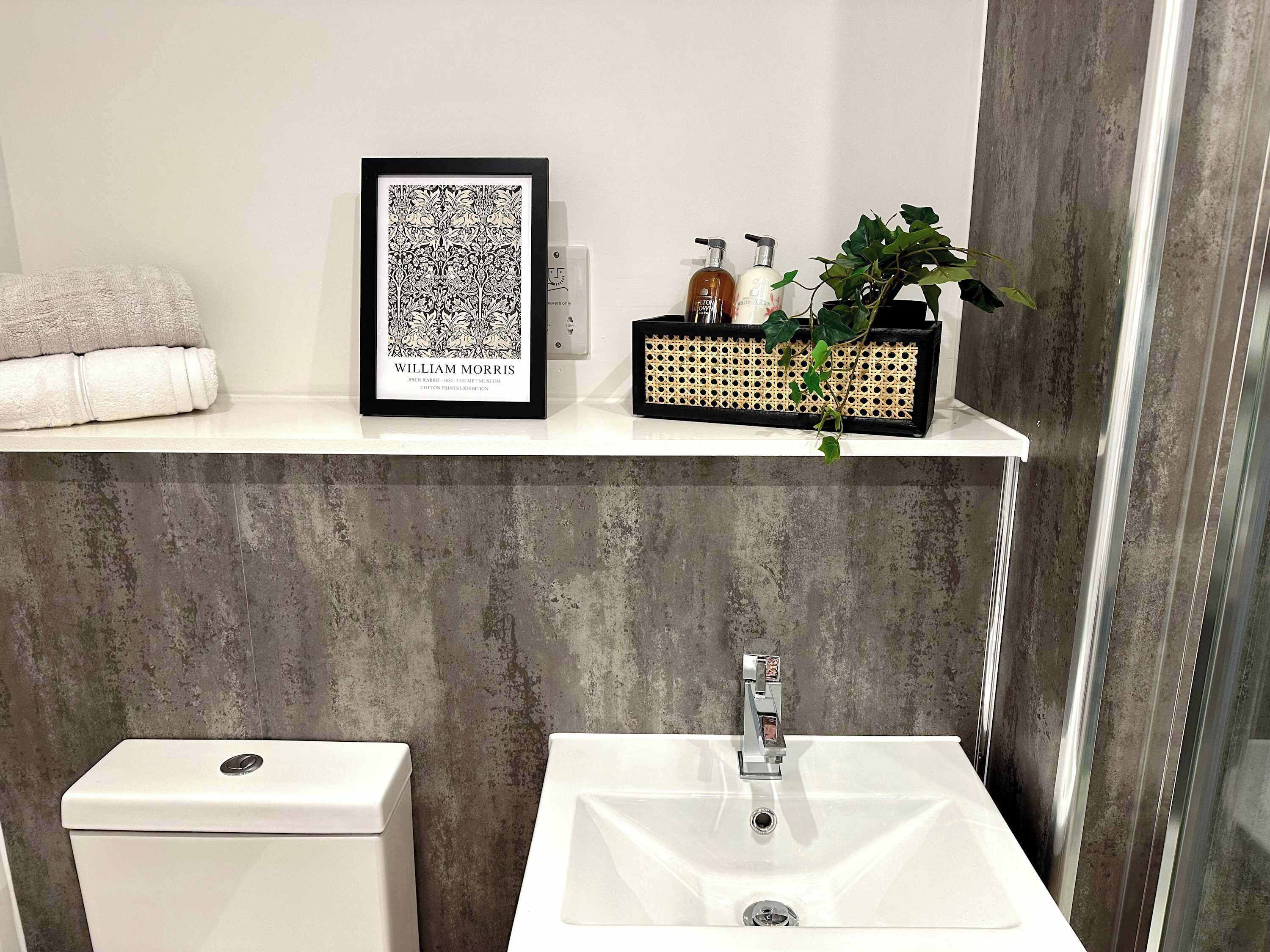 A bathroom with a toilet, sink, framed artwork, toiletries, and a potted plant.