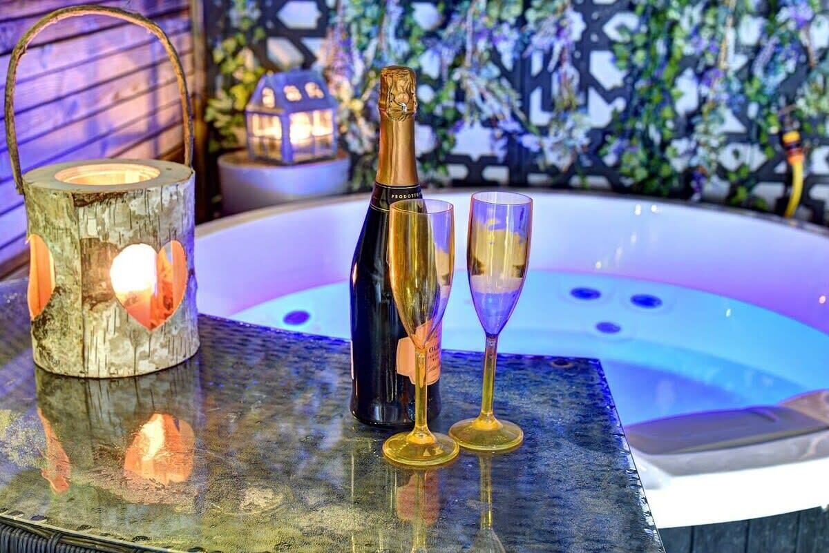 A bottle of champagne, two glasses, and a rustic lantern on a reflective surface.
