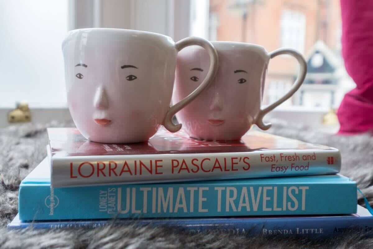 Two ceramic mugs with faces on a stack of books.