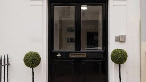 A black door with a glass panel, flanked by two spherical topiary plants, and a small mailbox on the door. - Host & Stay | Bedford Place Hideaway (Brighton and Hove)