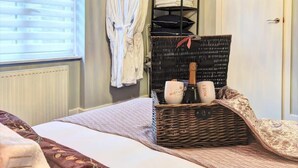 A neatly made bed with a brown and white patterned bedspread, a wicker basket with two Moët & Chandon champagne glasses, and a white robe hanging on a rack. - Host & Stay | Bedford Place Hideaway (Brighton and Hove)