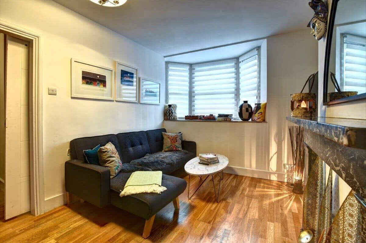 A living room with a dark-colored sofa, a small round table, and a bay window with blinds.