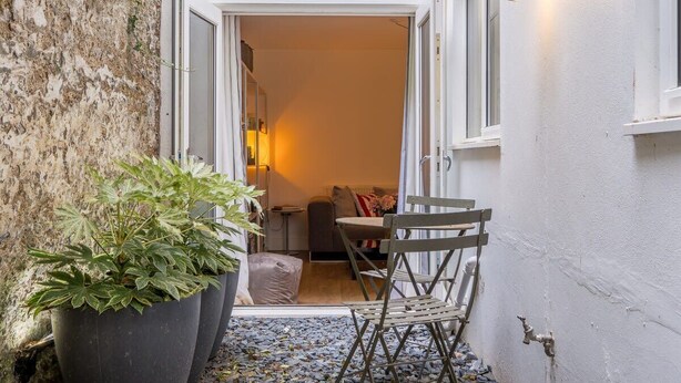 A narrow outdoor space with a potted plant, a folding chair, and a doorway leading to an interior room with a sofa and a lamp. - Host & Stay | Osbourne Rest (Brighton and Hove)