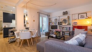 A modern living room with a grey sofa, a coffee table, and a bookshelf. There is a dining area with a table and chairs. - Host & Stay | Osbourne Rest (Brighton and Hove)