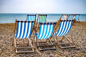 Beach chairs with striped blue and white fabric, arranged on a pebbled beach with the sea in the background.