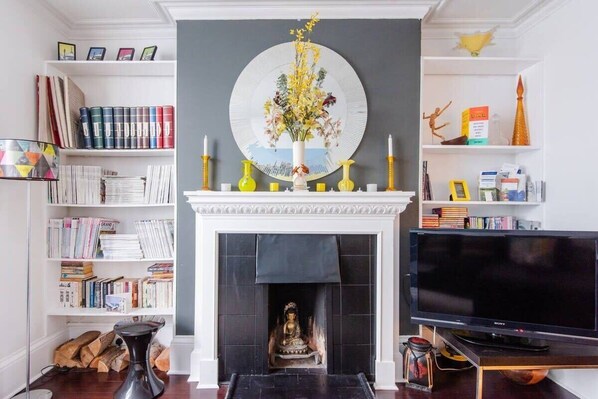 A living room with a fireplace, a television, and bookshelves filled with books and decorative items.