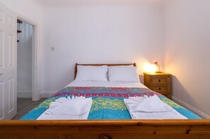 Uma cama bem arrumada com um edredom colorido, uma luminária de cabeceira e um criado-mudo de madeira.