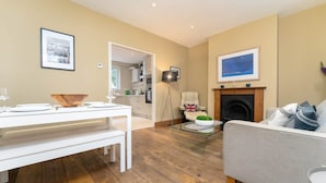 Un salon moderne comprenant un coin repas, une cheminée et une cuisine visible à travers une porte ouverte.
