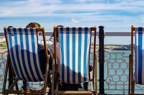 Two striped beach chairs facing a railing with a view of the sea and buildings in the distance.