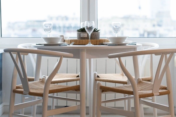 A round dining table with white chairs, a small potted plant, and two wine glasses.