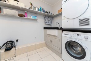 A laundry room with a Bosch washing machine, a vacuum cleaner, and shelves with various items.