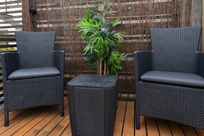 Two wicker chairs with cushions, a small square table, and a bamboo plant in a wooden deck area.