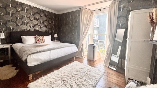 Una camera da letto con un letto grande, un comodino, una cassettiera, un tappeto soffice e vista sull'esterno attraverso una finestra.