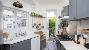 Eine kleine Küche mit Gasherd, weißen Schränken und einem Fenster mit Blick auf einen Garten.