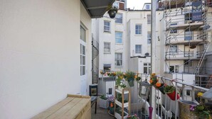 Ein schmaler Balkon mit Holzbanken, Blumentöpfen und einem Metallgeländer.
