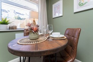 A dining area with a round wooden table, a brown leather chair, a woven placemat, a decorative vase, a wine glass, and a white bowl. - Host & Stay | Round Hill Apartment (Brighton and Hove)