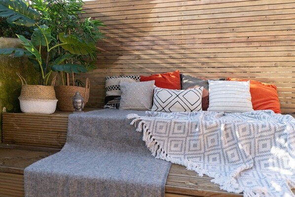 A wooden deck with a bench, cushions, and a blanket.