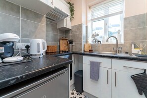 A modern kitchen with grey tiles, a built-in oven, a coffee machine, and a window with a view.