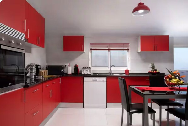 Une cuisine moderne avec des meubles rouges, une cuisinière noire et un luminaire suspendu rouge.