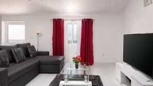 A modern living room with a sectional sofa, a glass coffee table, a flat-screen TV, and red curtains. - Calheta Ocean View Retreat - Casa Santana (Estreito da Calheta)
