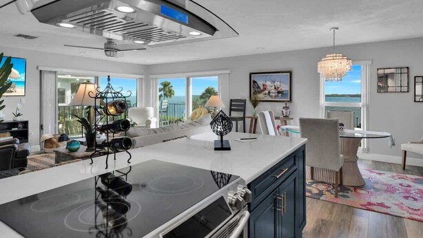 A modern kitchen with a central island, stainless steel range hood, and large windows offering a view of the outdoors. - Waters Edge (Marathon)