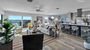 A spacious living area with a large window, a ceiling fan, and a kitchen area with bar stools. - Waters Edge (Marathon)