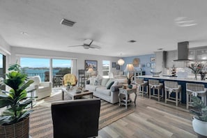 A spacious living area with a large window, a ceiling fan, and a kitchen area with bar stools. - Waters Edge (Marathon)