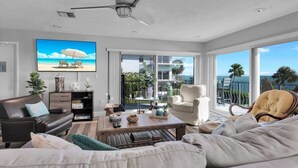 A spacious living room with a large TV, comfortable seating, a ceiling fan, and a balcony with a view of the ocean. - Waters Edge (Marathon)