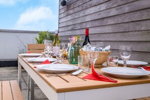 Une table à manger installée à l’extérieur, avec des assiettes, des couverts, des verres et des bouteilles.