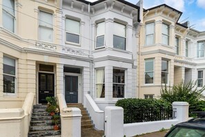A row of white terraced houses with a central entrance, steps, and a black car parked in front.