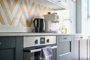 A modern kitchen with a digital clock, a coffee machine, and a patterned backsplash.