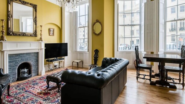 Ein Wohnzimmer mit Kamin, einer schwarzen Ledersofa, einem Chandelier und großen Fenstern.
