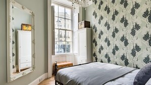 Ein Schlafzimmer mit Bett, einem großen Spiegel, einem Kleiderschrank und einem Fenster mit Blick auf Gebäude.
