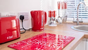 A kitchen counter with a red Russell Hobbs toaster, a red kettle, and a red coffee maker. There are kitchen utensils and a red placemat with food-related words. - Host & Stay | Wilson Studio (Brighton and Hove)
