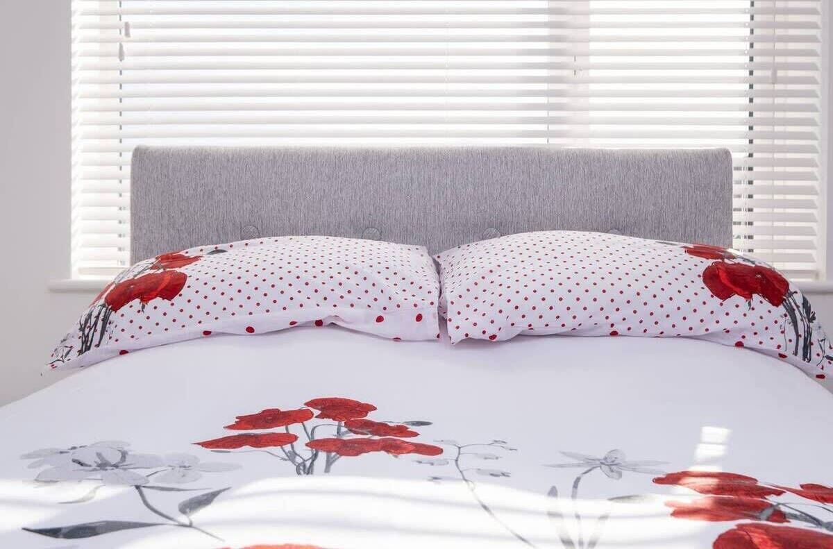 A bed with a white duvet featuring red floral patterns, a grey headboard, and white blinds in the background.