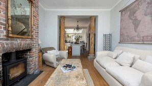 A living room with a fireplace, a sofa, a coffee table with magazines, and a kitchen in the background. - Host & Stay | The Walpole House (Brighton and Hove)