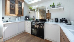 A modern kitchen with white cabinets, a black stove, and wooden upper cabinets. There are plants on shelves and a skylight above. - Host & Stay | The Walpole House (Brighton and Hove)