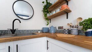 A kitchen with a black sink, white cabinets, a wooden countertop, a round mirror, and shelves with kitchenware and plants. - Host & Stay | Islingword Studio (Brighton and Hove)